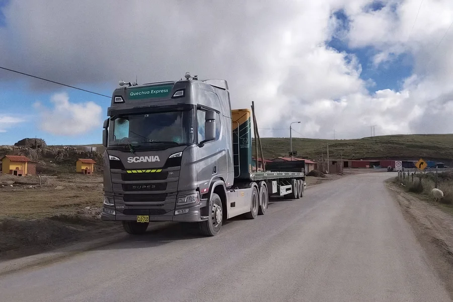 Tracto Scania Super de Quechua Express con plataforma, cruzando un caserío de la puna camino a Chumbivilcas